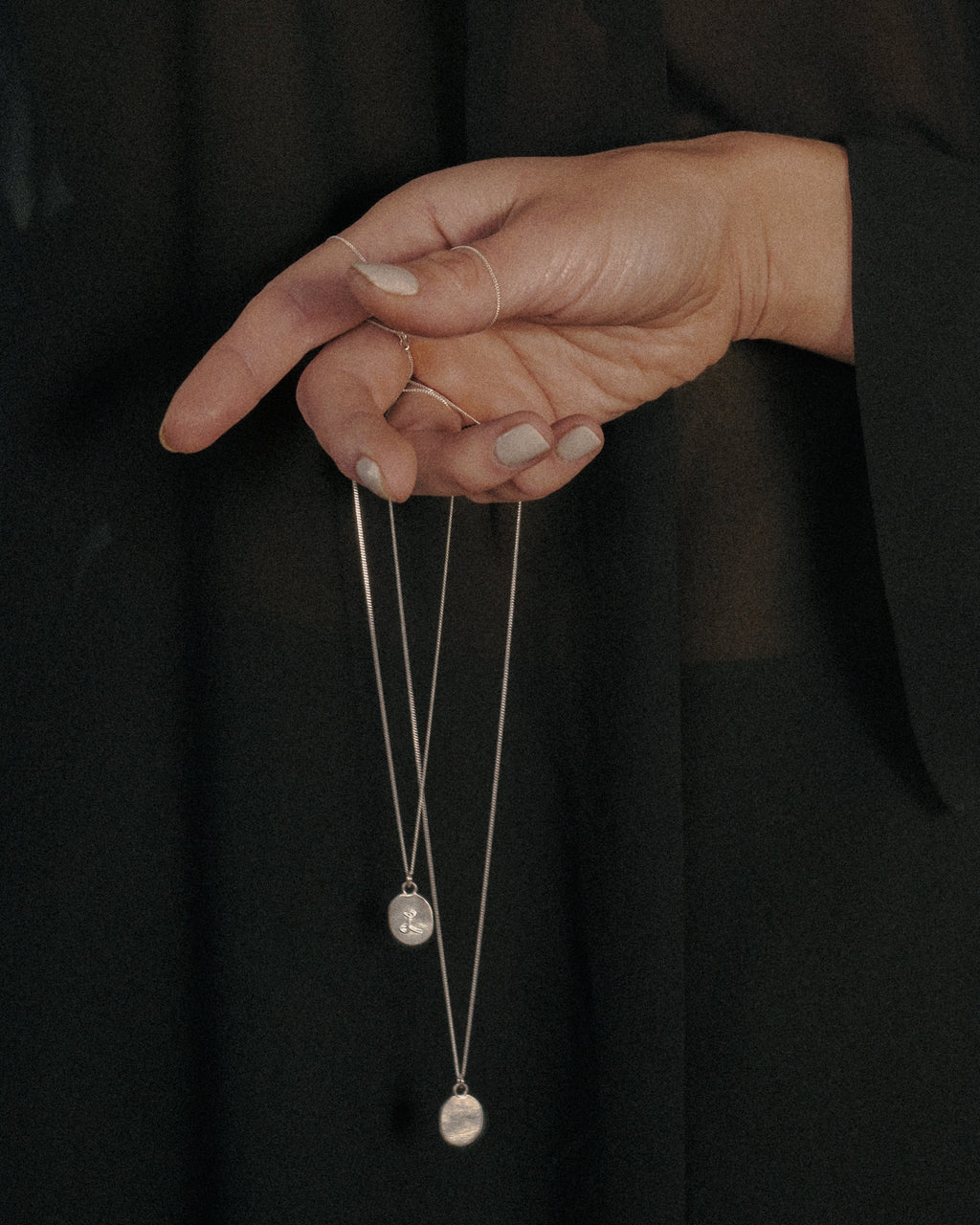 Hand holding a necklace with two initial pendants against a dark background