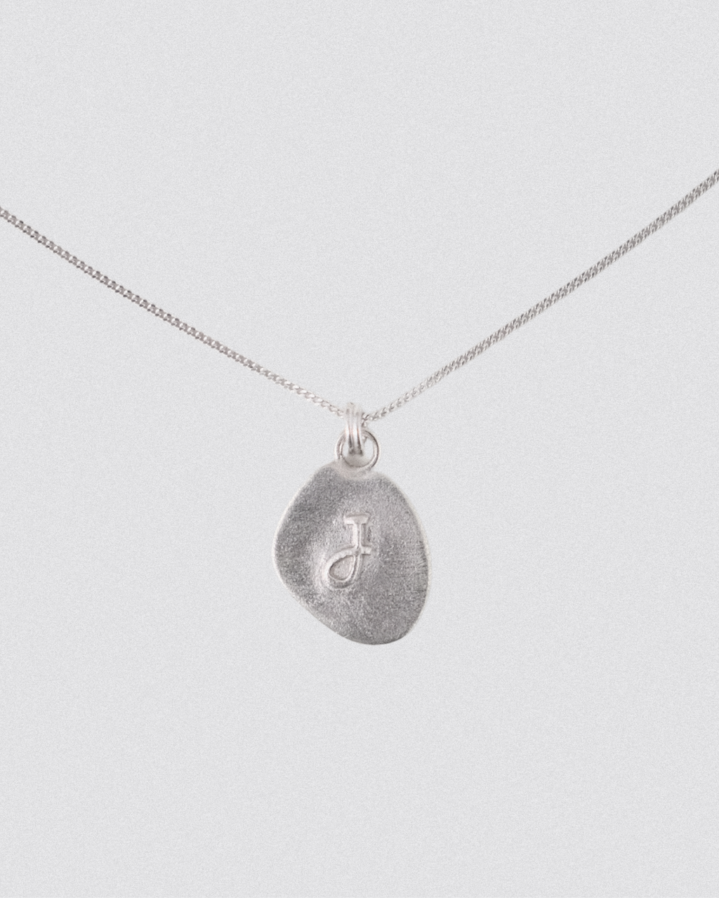 Silver Pebble shape necklace with a textured pendant on a light gray background