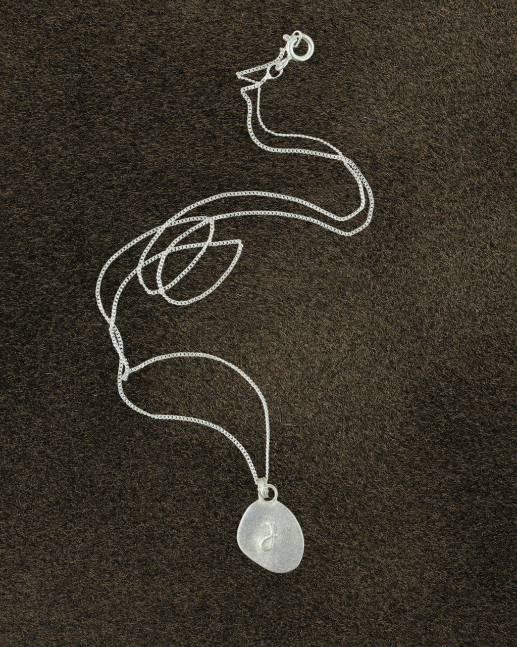 Silver Pebble shape necklace with a pendant on a dark brown textured background