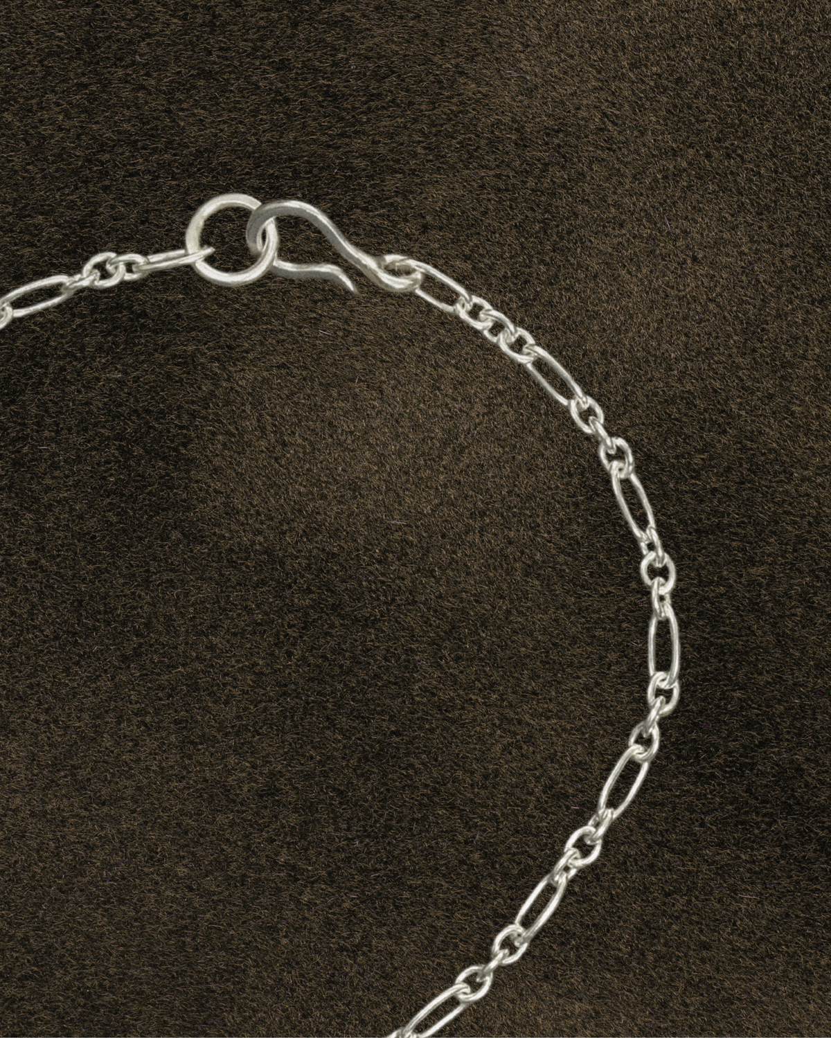 Silver chain figaro bracelet with s hook clasp on a dark brown background