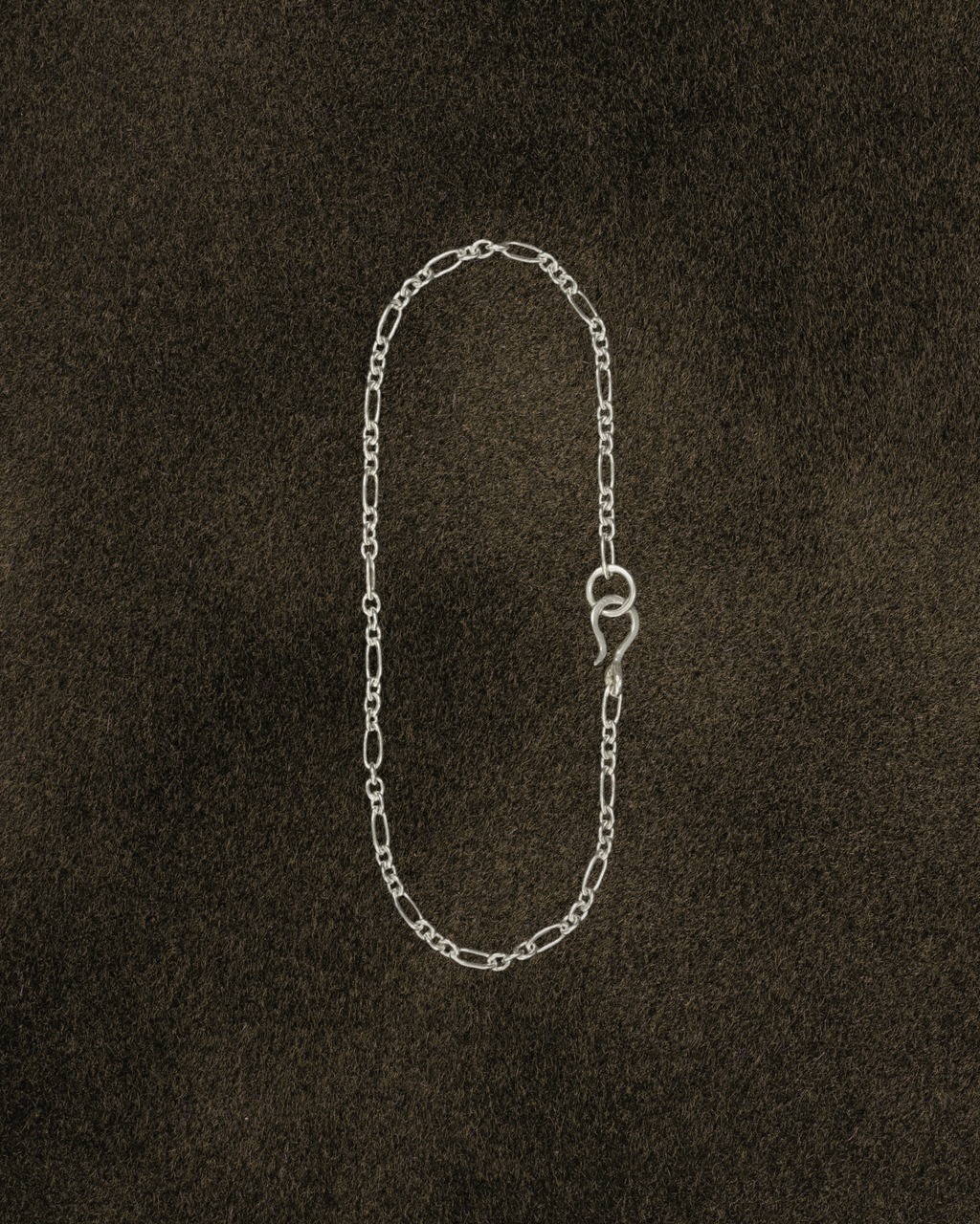 Silver figaro chain bracelet with s hook clasp on a dark brown textured background