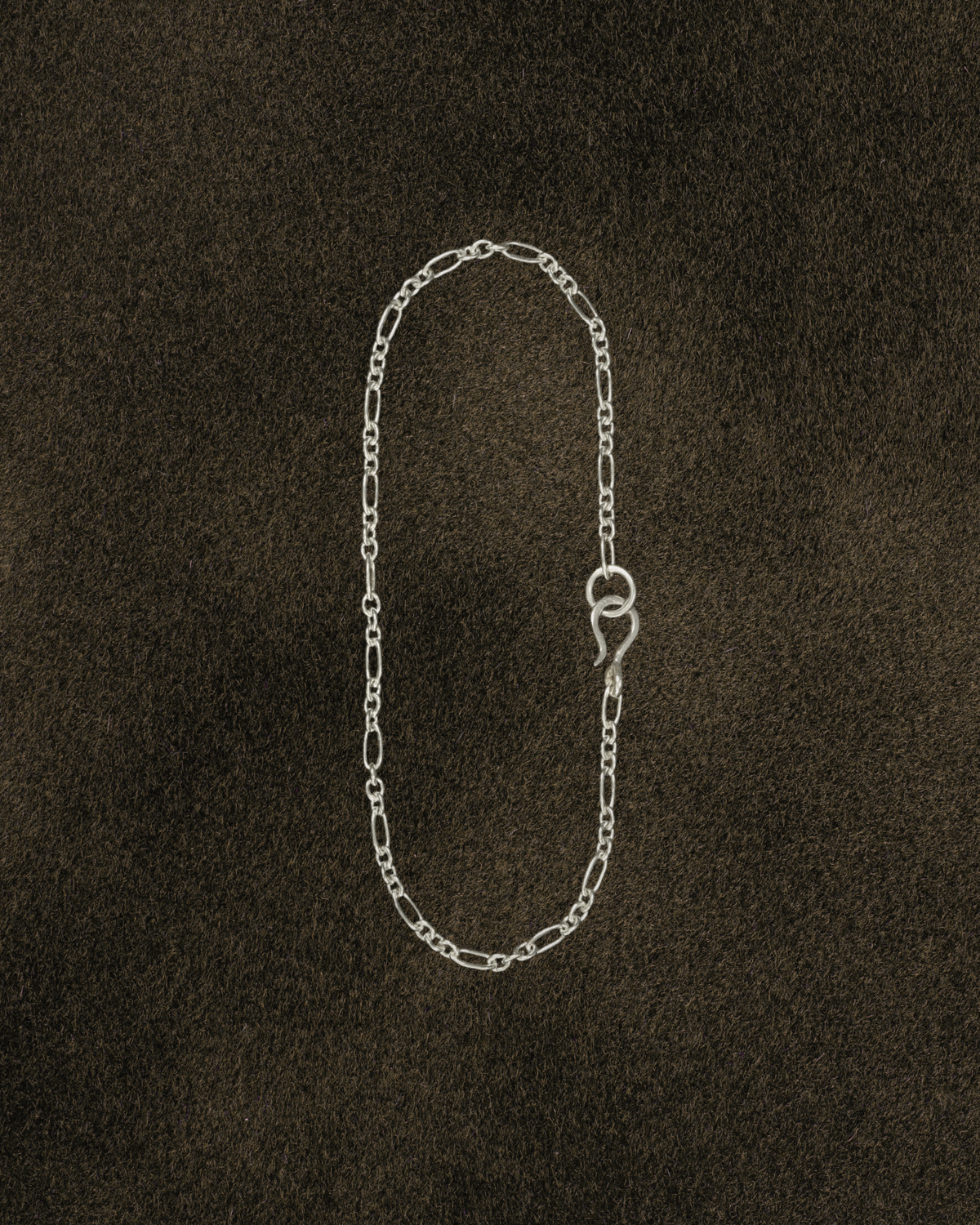 Silver figaro chain bracelet with s hook clasp on a dark brown textured background