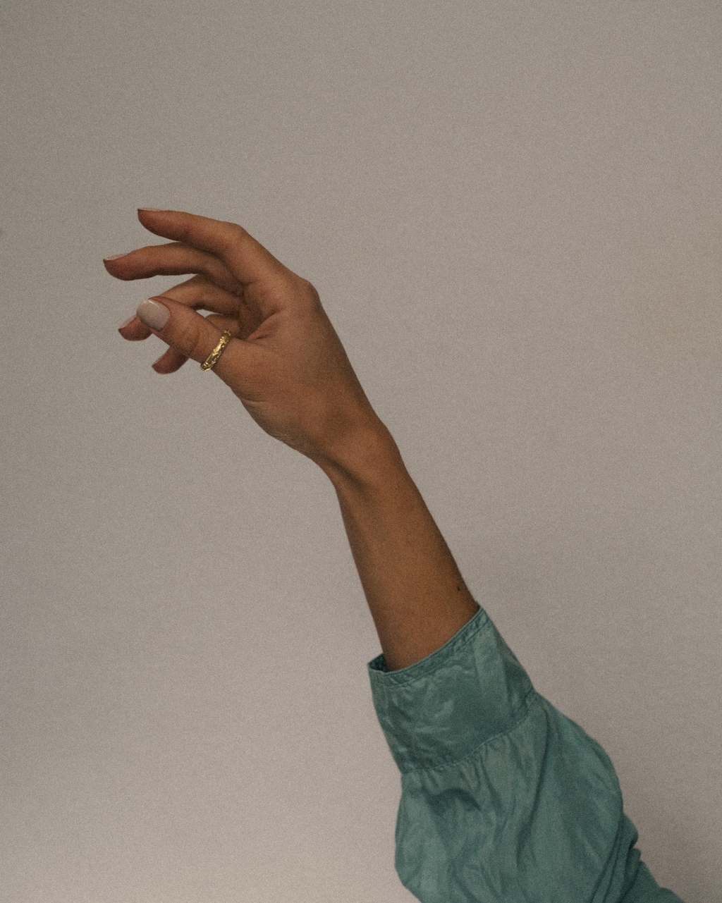 Hand raised with a gold leafy olive branch ring on a plain background