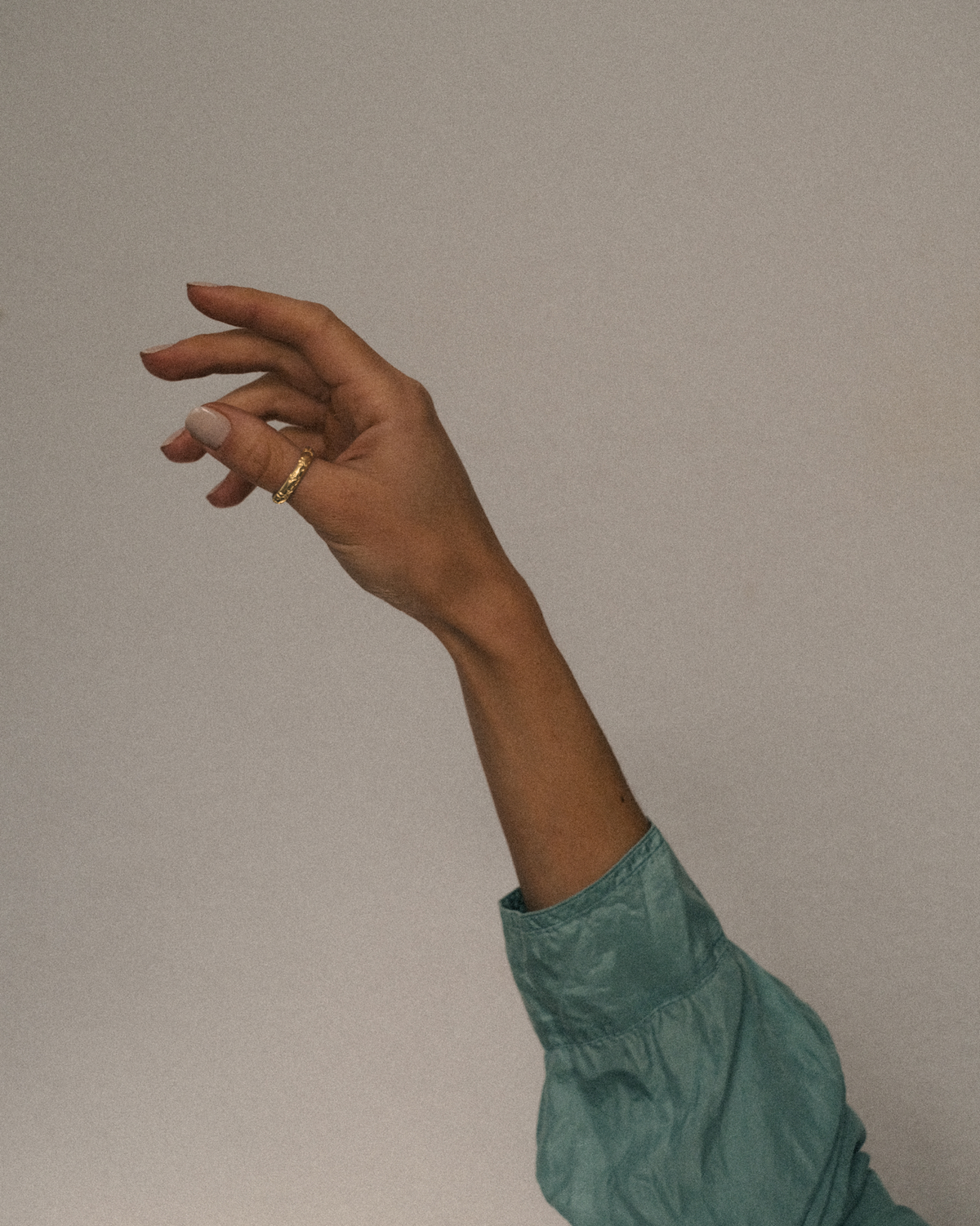 Hand raised with a gold leafy olive branch ring on a plain background