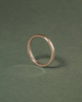 A hazelnut gold court band ring standing upright on a dark green textured background.