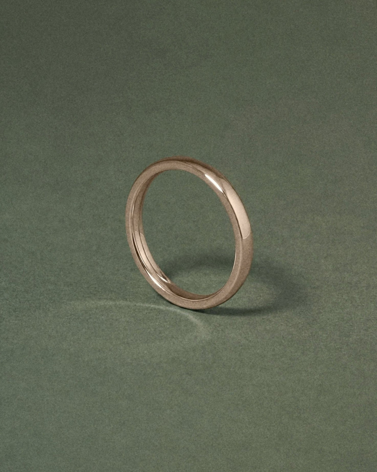 A hazelnut gold court band ring standing upright on a dark green textured background.