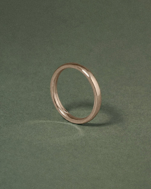 A hazelnut gold court band ring standing upright on a dark green textured background.