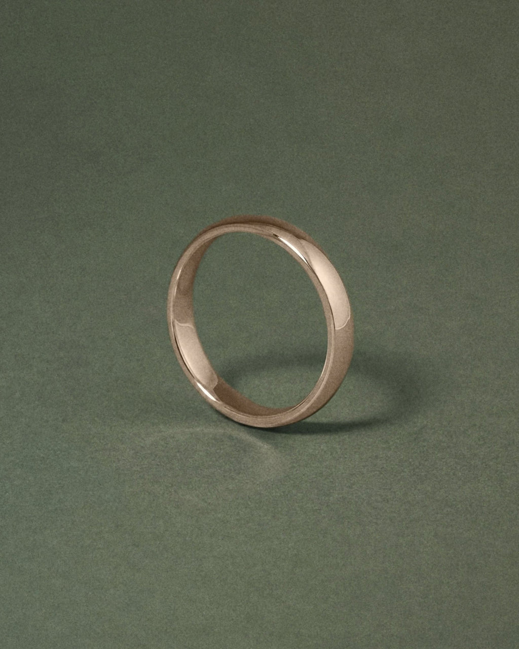 A minimalist hazelnut gold court band ring standing upright on a dark green textured background.