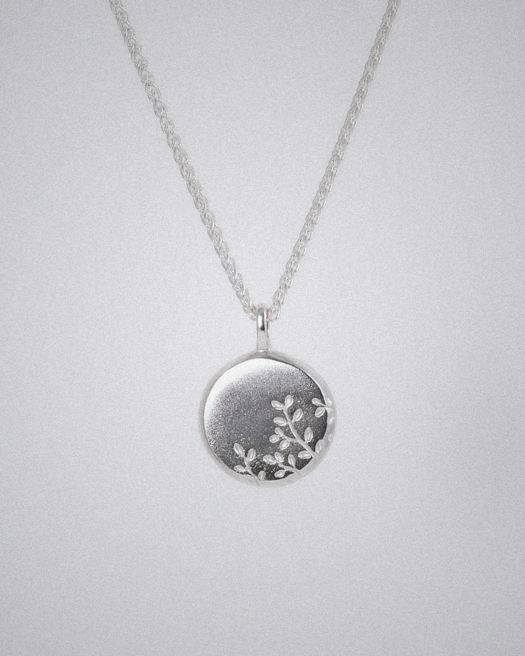Silver necklace with a round pendant and olive branch engraving on a light gray background