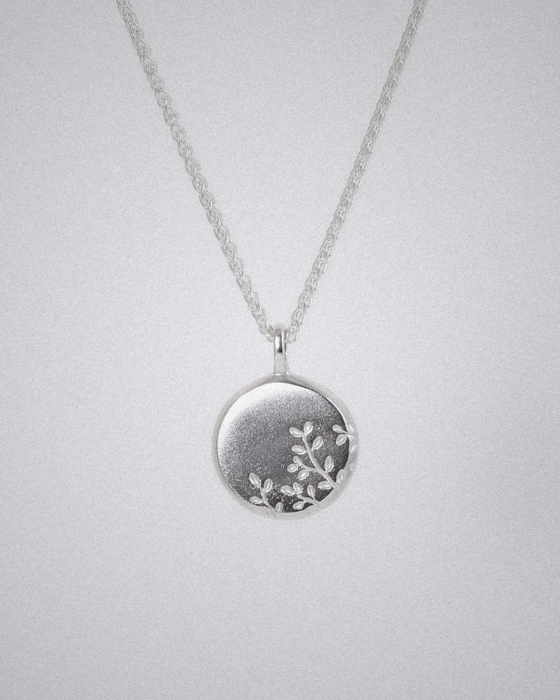 Silver necklace with a round pendant and olive branch engraving on a light gray background